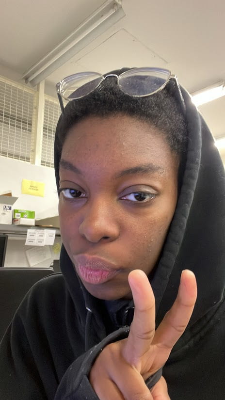 young person in a dark hoodie with glasses on top of their head, flashing a peace sign.